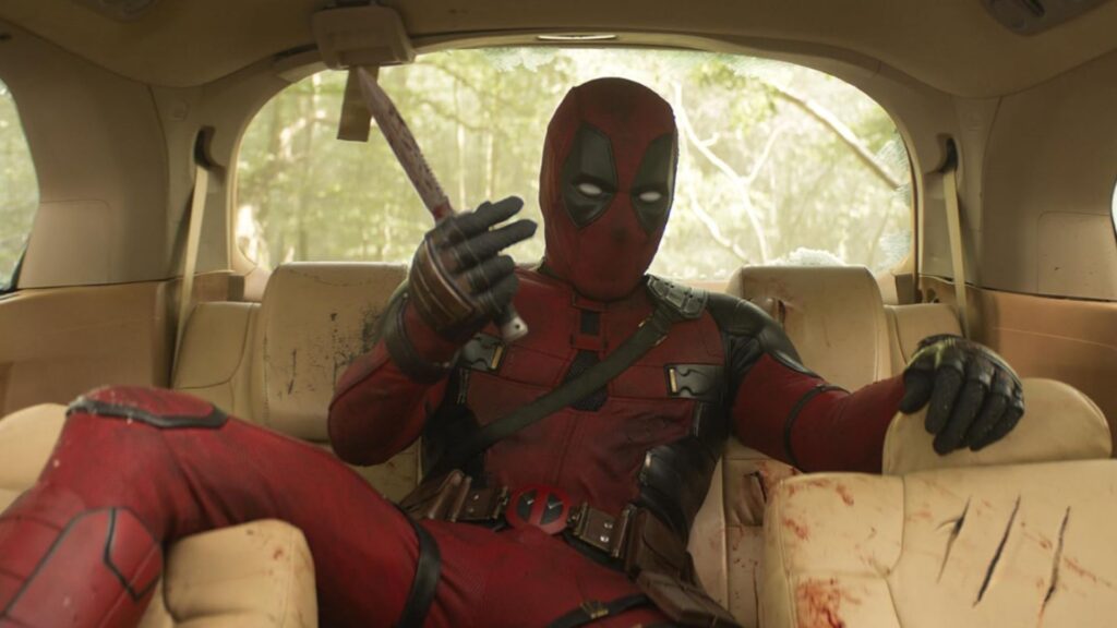 Deadpool sitting inside a car with a hammer in his hand